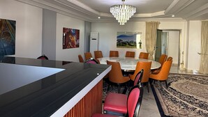 Een moderne eetruimte met een ronde tafel, oranje stoelen, een zwart aanrecht en een kroonluchter.