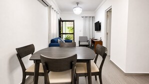 En matplats med ett bord och stolar, en soffa, en tv och ett fönster med gardiner.