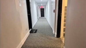 A hotel hallway with carpeted floors, doors on both sides, and a red light at the end. - Miami Beach Quaint Studio  (Miami Beach)