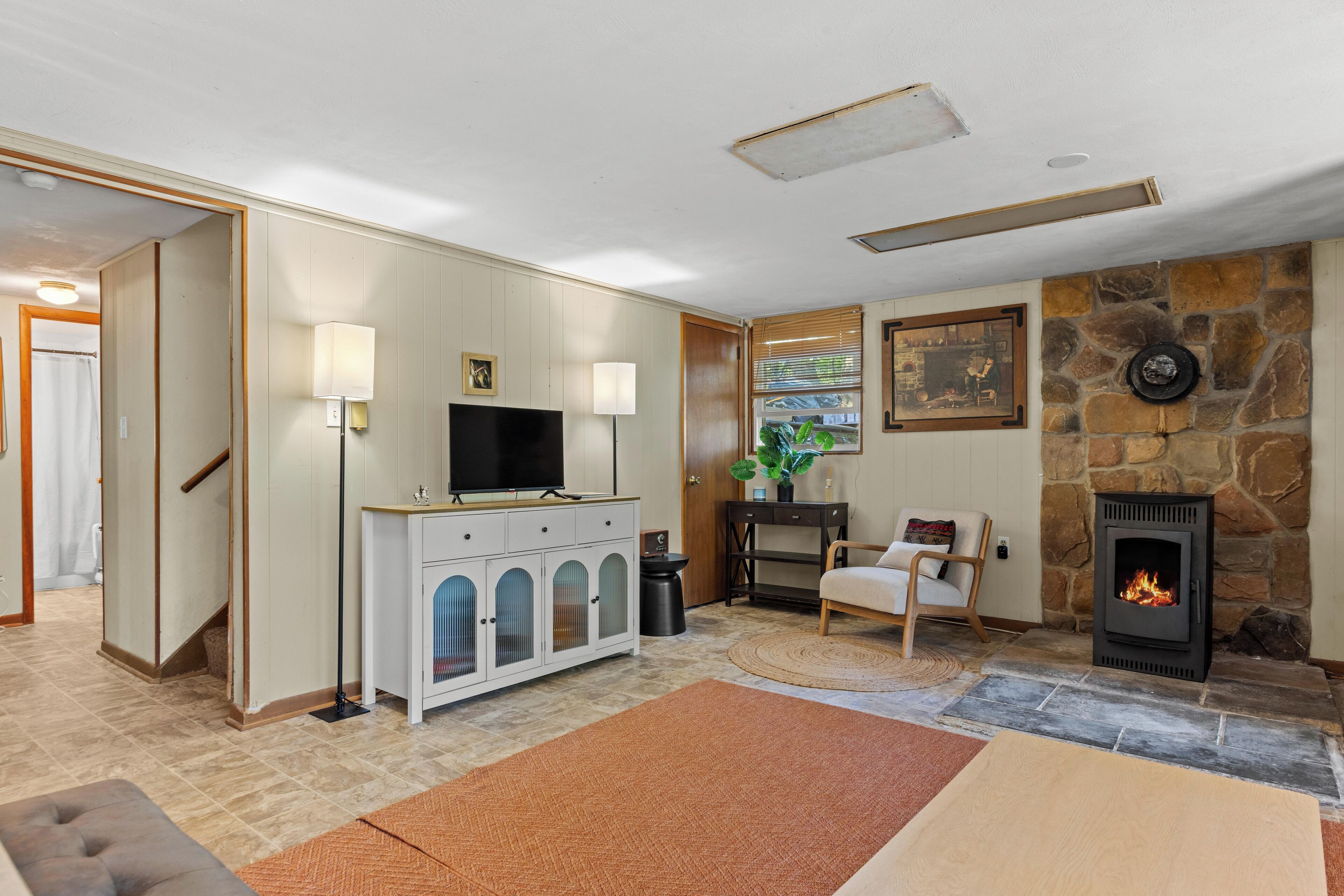 A living room with a stone fireplace, a television on a cabinet, and a door leading to another room.