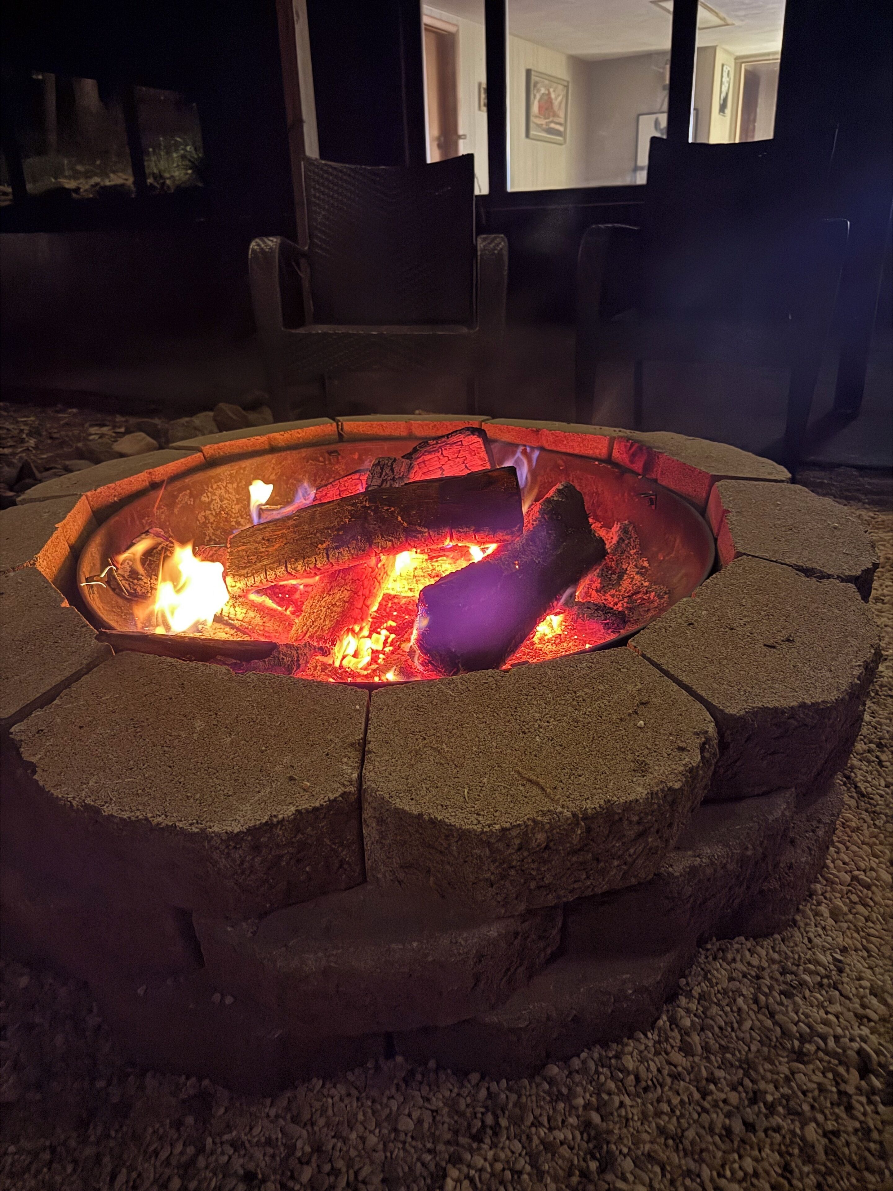 A stone fire pit with burning logs, surrounded by a pebble ground.