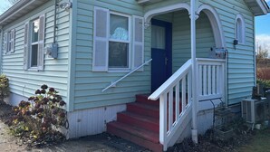 Ein kleines, eingeschossiges Haus mit einer Veranda, einer blauen Tür und einem roten Podest.