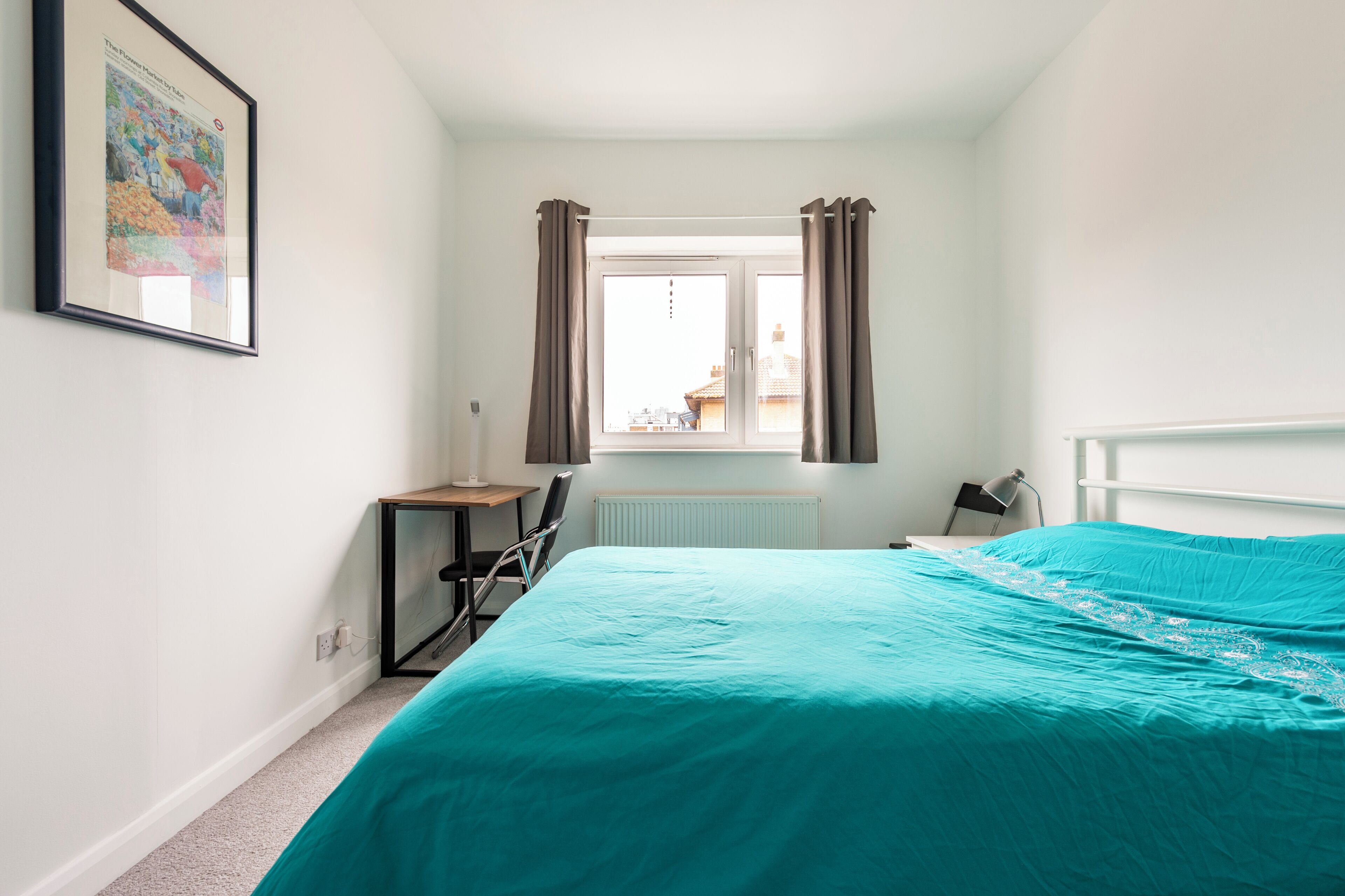 A bedroom with a bed, a desk, a chair, a radiator, and a window with curtains.