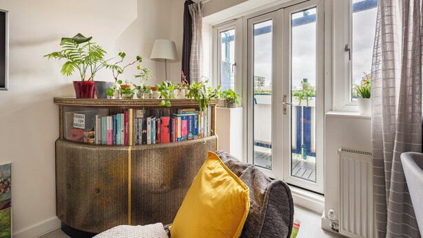 A living room with a sofa, a bookshelf, and a view of the outside. - 1 Bedroom flat in Trendy East London (London)