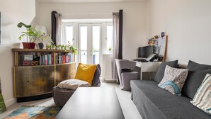 A modern living room with a sofa, a coffee table, a bookshelf, and a desk with a computer. - 1 Bedroom flat in Trendy East London (London)