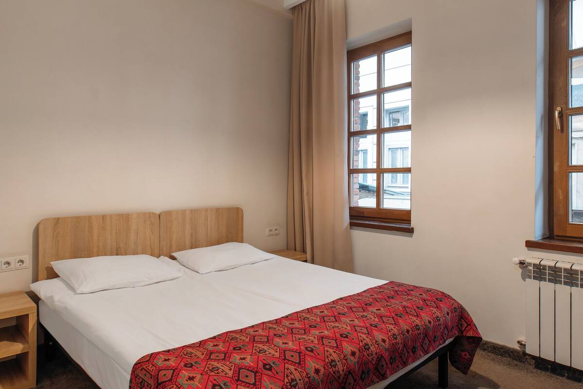 A bedroom with a bed, a nightstand, a window, and a radiator.