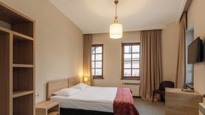 A hotel room with a bed, a desk, a chair, a TV, and a window with curtains. - Tekla Palace Block B by Urban Hotels  (Tbilisi)
