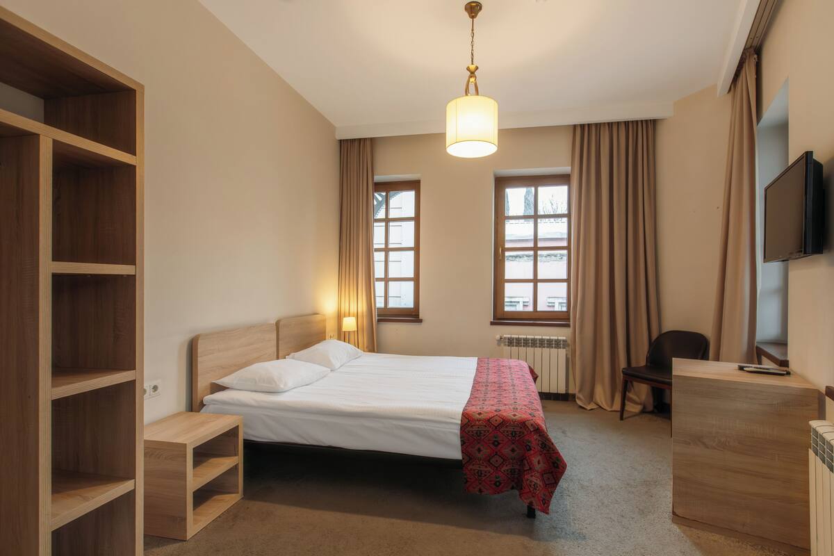 A hotel room with a bed, a desk, a chair, a TV, and a window with curtains.