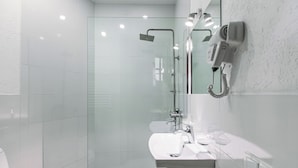A modern bathroom with a glass-enclosed shower, a white sink, and a hairdryer mounted on the wall. - Tekla Palace Block B by Urban Hotels  (Tbilisi)