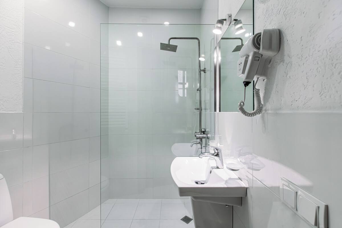A modern bathroom with a glass-enclosed shower, a white sink, and a hairdryer mounted on the wall.