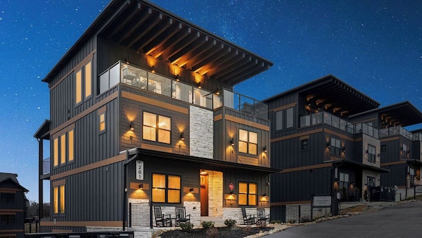 A modern multi-story residential building with a balcony, large windows, and a well-lit entrance. - Evergreen Escape - Luxury Rooftop - Indoor Pool - Home Theater - Game Rooms (Sevierville)
