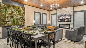 A dining area with a long table set for six, surrounded by chairs, a fireplace, and a television mounted on the wall. - Evergreen Escape - Luxury Rooftop - Indoor Pool - Home Theater - Game Rooms (Sevierville)