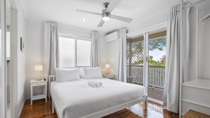Un dormitorio con cama, ventilador de techo, ventana, mesita de noche y vistas al exterior.