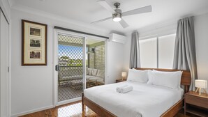 Un dormitorio con una cama de madera, un ventilador de techo, una puerta corrediza de vidrio que da a un área exterior y un cuadro en la pared.