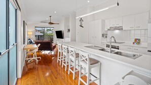 Una cocina moderna con armarios blancos, una isla central con taburetes y un amplio ventanal con vistas a un jardín.