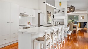 Una cocina moderna con armarios blancos, una isla central con taburetes y un comedor con vistas al exterior.
