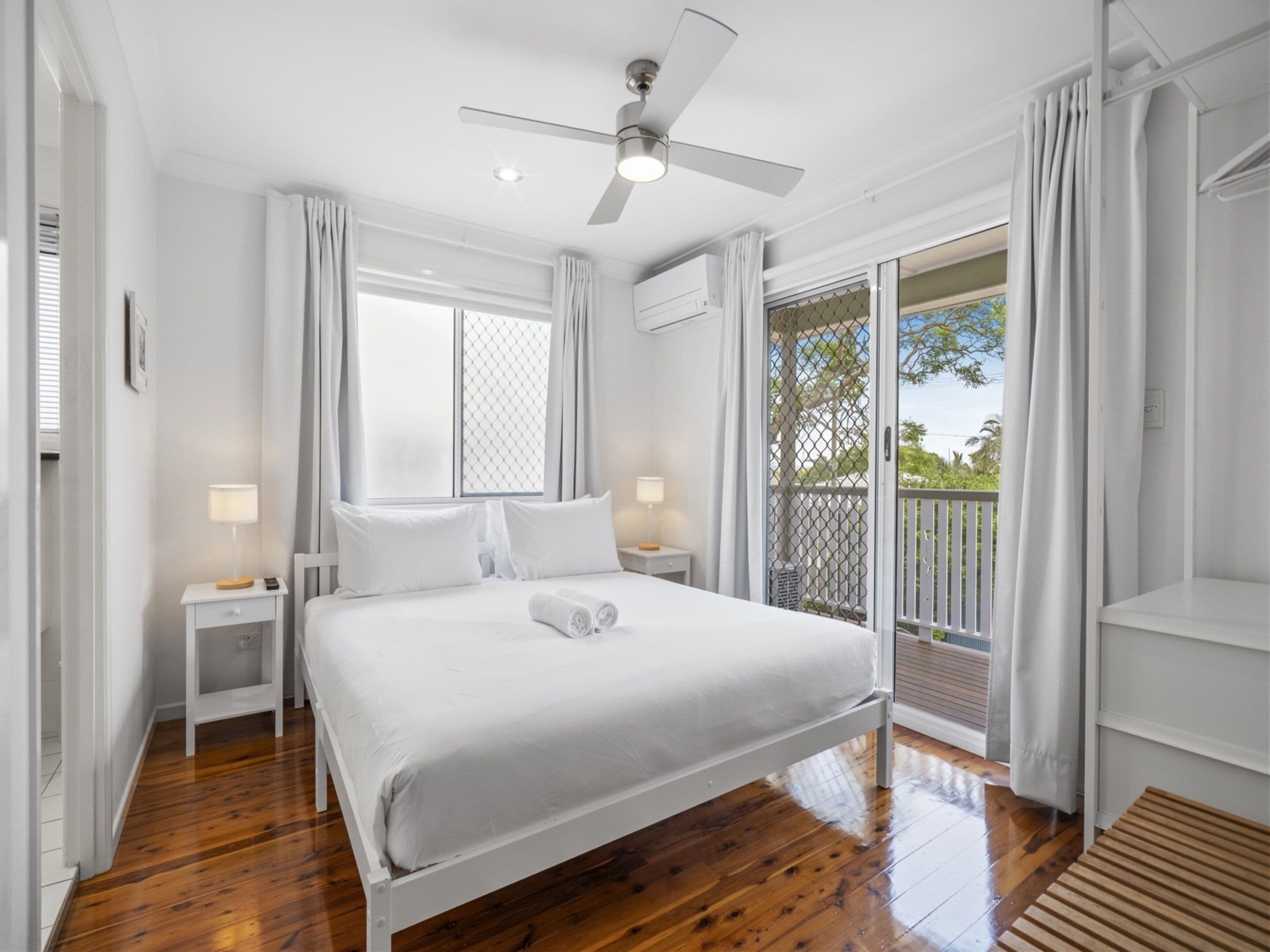 A bedroom with a bed, nightstands, a ceiling fan, and a view through a sliding glass door.