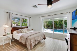 Un dormitorio con cama, mesita de noche, lámpara y vista a una piscina.