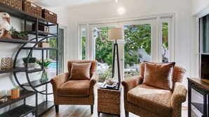 A living room with two patterned armchairs, a floor lamp, a bookshelf, and a large window with a view of greenery. - Sunny Deerfield Beach Oasis w/ Pool & Canal Views (Deerfield Beach)