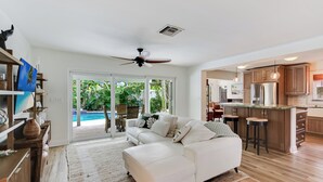 A spacious living room with a white sofa, a ceiling fan, and a large sliding glass door leading to a pool. - Sunny Deerfield Beach Oasis w/ Pool & Canal Views (Deerfield Beach)
