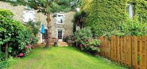 A stone house with a wooden deck, a wooden fence, and a variety of plants and flowers. - GARANCE gîte for 1 to 6 people (Taden)