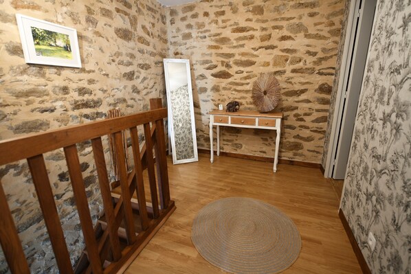 A room with a wooden floor, a round woven rug, a wooden bench, a small table with a decorative item, a mirror, and a picture on the wall. - GARANCE gîte for 1 to 6 people (Taden)