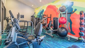 Une salle de sport équipée de matériel d’exercice, ornée d’une fresque colorée et dotée d’un tapis bleu.