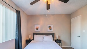 Une chambre à coucher avec un lit, deux tables de chevet, un ventilateur de plafond et des œuvres d’art accrochées au mur.