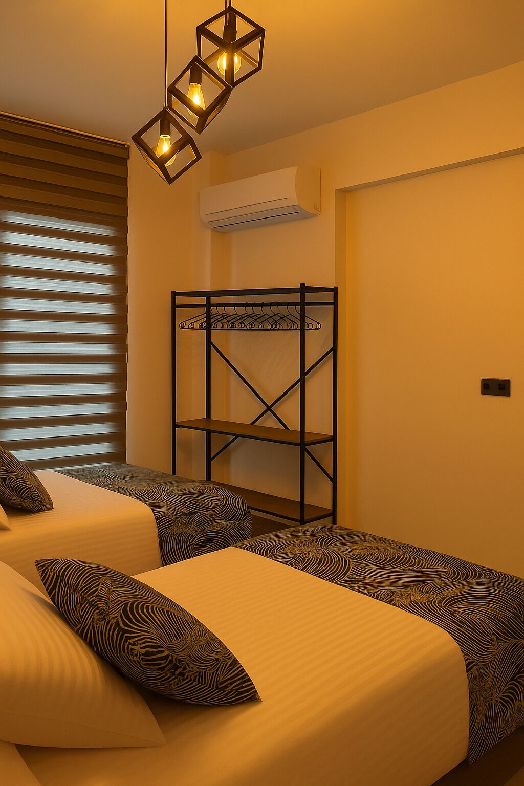 A bedroom with two beds, a bunk bed, a hanging light fixture, and a window with blinds.