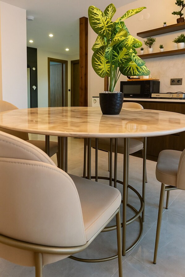 Ein moderner Essbereich mit einem runden Tisch, zwei beigen Stühlen und einem Blumentopf mit gefleckten Blättern.