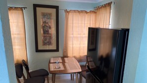 Een kleine eethoek met een tafel, stoelen, een koelkast en een televisie.