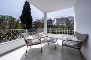 Un balcon agrémenté de meubles en osier, d’une table et offrant une vue sur un immeuble et des arbres.