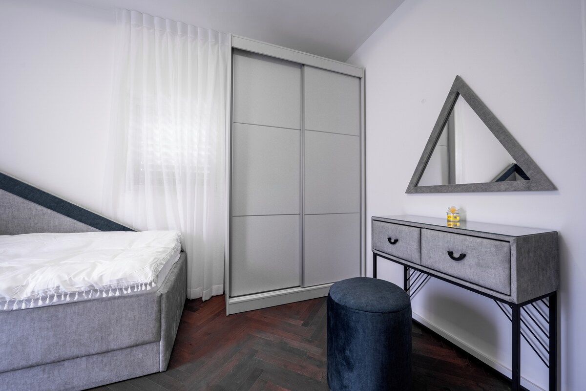 A bedroom with a bed, a wardrobe, a vanity with drawers, a mirror, and a stool.