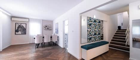 A spacious living area with a herringbone wood floor, a dining table with chairs, a large abstract painting, and a staircase leading to another level.