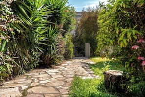A stone pathway leading through a lush garden with dense foliage on both sides.