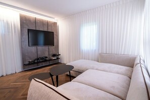 Una sala moderna con un televisor de pantalla plana montado en la pared, un sofá, una mesita y un suelo de madera con patrón de espiga.