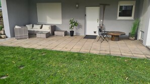Een overdekt terras met tuinmeubilair, een deur en een raam.