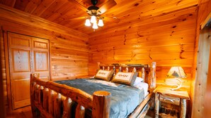 A wooden cabin bedroom with a bed, a nightstand, a lamp, and a ceiling fan.