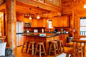 A wooden cabin interior with a kitchen, bar stools, and a large wooden pillar. - Gray Wolf Lodge | Hocking Hills, Luxury Log Cabin (South Bloomingville)