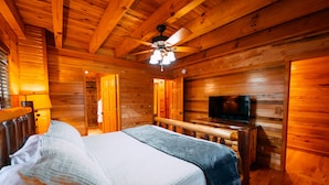 A wooden cabin room with a bed, a television, and a ceiling fan.