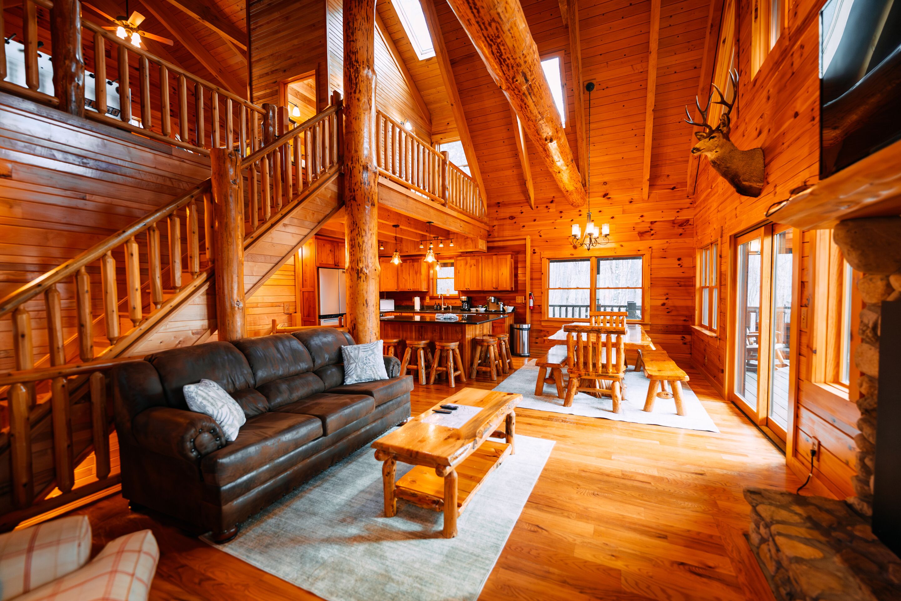 L’intérieur d’une cabane en rondins, avec un escalier, des meubles en bois et une tête d’animal empaillée accrochée au mur.