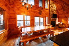 Ein Holzblockhaus-Interieur mit einem großen Holzesstisch, Bänken, einem Steinkamin und einem aufgehängten Hirschkopf.