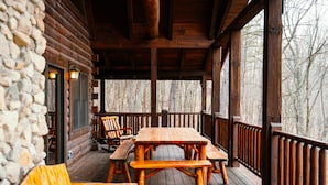 A wooden deck with a picnic table and benches, a stone wall, and a view of trees.