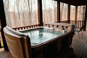 A hot tub on a wooden deck with a view of leafless trees. - Gray Wolf Lodge | Hocking Hills, Luxury Log Cabin (South Bloomingville)