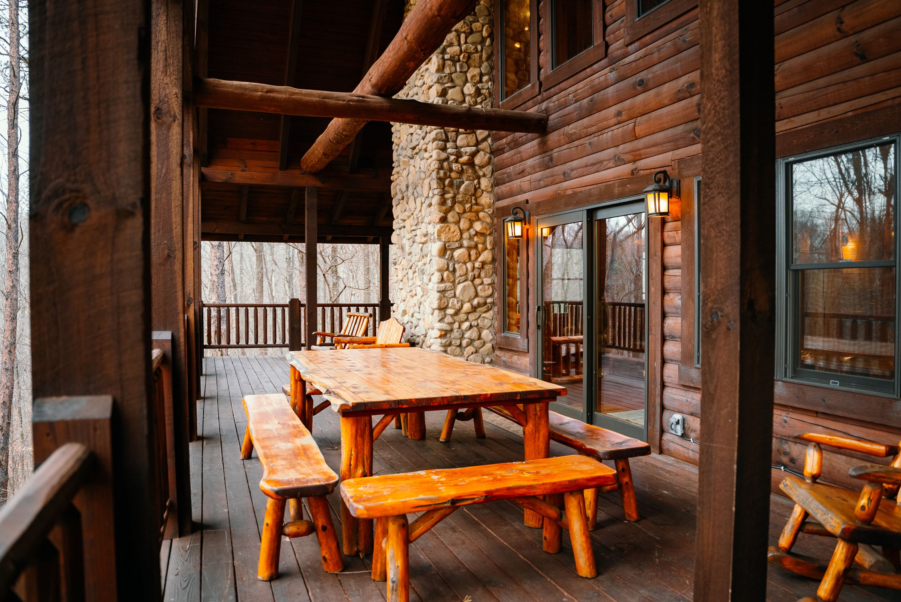 A wooden cabin with a stone pillar, wooden benches, and a large table.