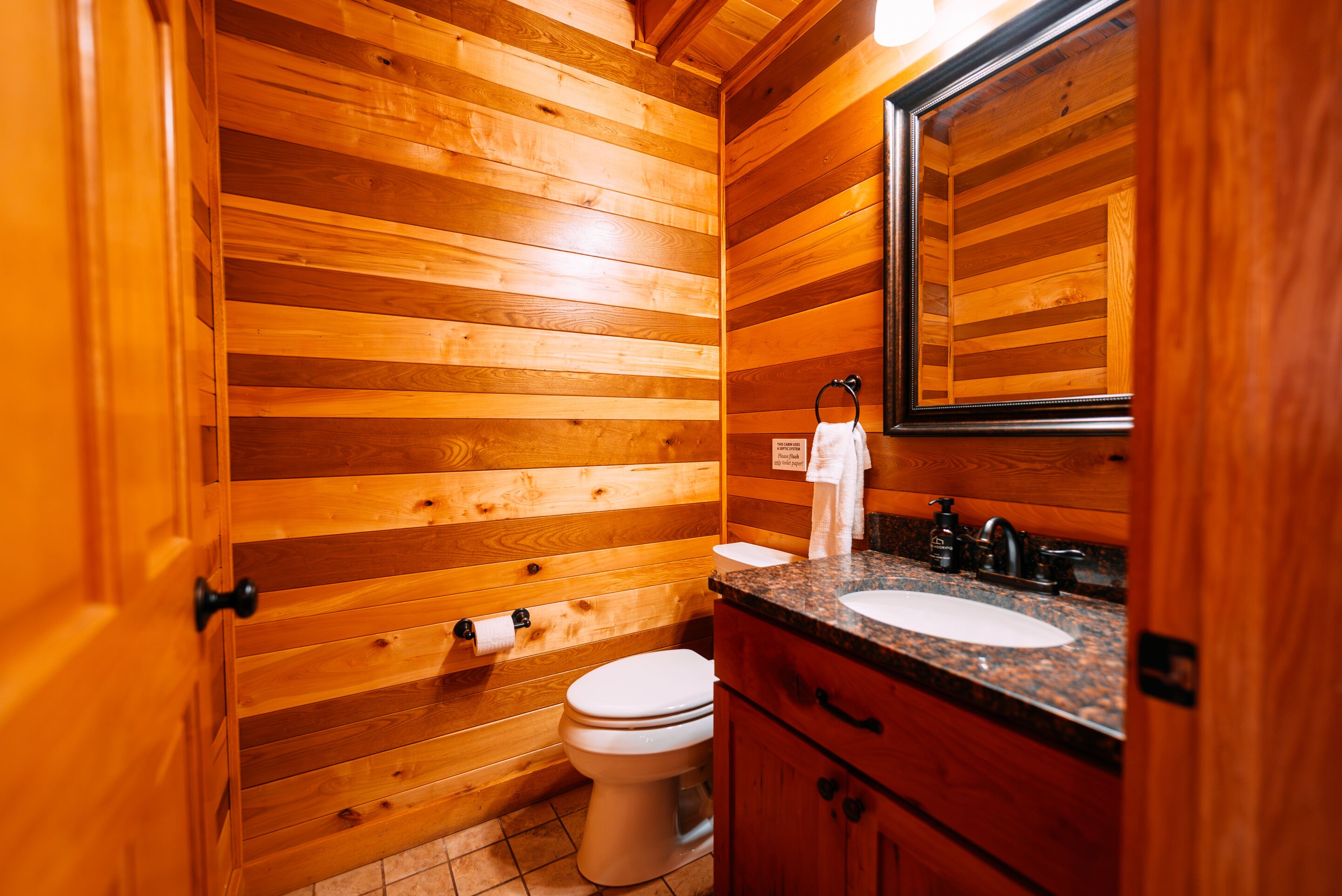 Un baño con paneles de madera, que incluye inodoro, lavamanos y espejo.