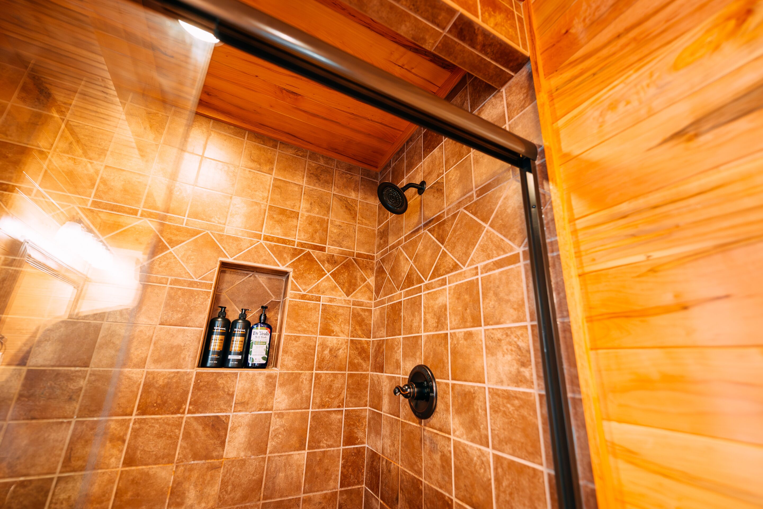 A shower area with tiled walls, a wooden ceiling, and a showerhead.