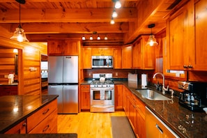 Interior de una cabaña de madera con cocina, que incluye un refrigerador, estufa, microondas y lavaplatos.