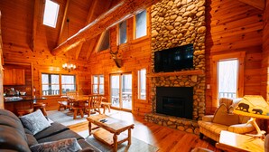 A log cabin interior with a stone fireplace, wooden furniture, and a television mounted on the wall.