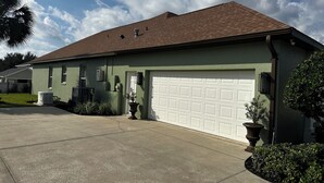 Een gelijkvloers huis met een groene gevel, een bruin dak en een witte garage.